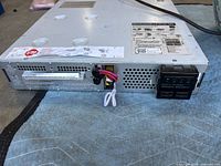 Overall view of APC Smart-UPS rack-mount UPS showing chassis, battery connector, wiring, and specification label