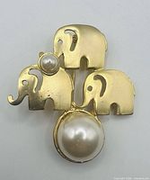 front view of brooch showing three gold tone elephants and two faux pearls