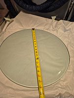 Top view of round glass tabletop with tape measure showing approximately 18 inch diameter