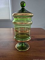 Full view of green glass apothecary jar with lid on pedestal displaying overall form and color