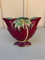 Front view showing burgundy body, raised gilt palm tree, and foot