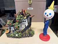 Cottage figurine beside Jack in the Box bobblehead front view