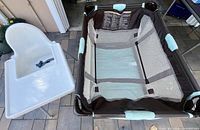 White IKEA high chair next to brown/aqua Graco playard folded open