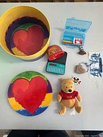 All items laid out on table including hat box, lid, plush, organizer, art kit, red dome toy, stone heart, sticker, book jacket