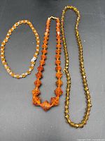 Three amber-tone necklaces on black background