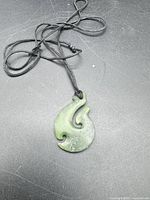 Front view of carved green jade pendant on braided cord