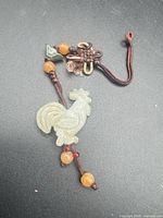 Full view of jade rooster charm with cord, knot, beads
