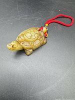 Front view of carved jade turtle pendant on red cord