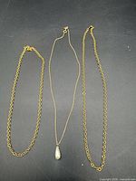 Three gold tone necklaces laid out: two cable chains and one fine chain with teardrop pendant