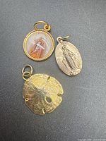 Three pendants laid out: oval Miraculous Medal, round religious image, sand dollar