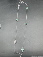 Full view of necklace showing alternating green and clear stone clover stations on silver-tone chain