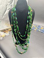 Full view of entire multi-strand green Murano glass necklace displayed on black bust