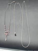 Three necklaces laid out: pink rhinestone chandelier pendant, red teardrop pendant, plain chain
