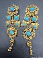 Full view of both articulated gold-tone filigree earrings with turquoise cabochons