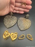 Overview of four pairs of earrings displayed on surface and hand