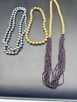 Three necklaces laid out: silver faux pearls, gold faux pearls, gold bead with tassel