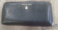 Front view of black pebbled leather wallet with Michael Kors logo and gold-tone zipper pull visible