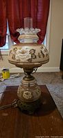 Front view of hurricane lamp showing floral glass shade, chimney, metal base