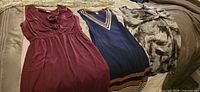 Burgundy, navy with striped neckline, and grey-black print sleeveless dresses laid out on bed