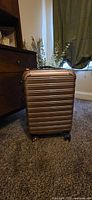 Front view of rose-gold hard-shell carry-on suitcase showing ribbed design and spinner wheels