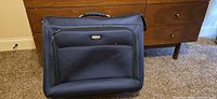 Front view of navy rolling garment bag with zip pocket and badge