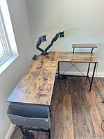 Full view of L-shaped desk showing woodgrain top, dual monitor arm, power strip, fabric bin