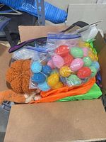 Box containing zipper bags of multicolour plastic Easter eggs, orange plush pumpkin, glimpse of inflatable