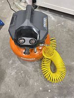 Top and front view of RIDGID 6-gallon pancake air compressor with attached yellow coiled hose