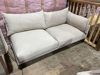 Front angled view of beige two-seat linen sofa showing cushions and legs