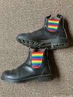 Side view of both boots showing black leather uppers, rainbow elastic panels and soles