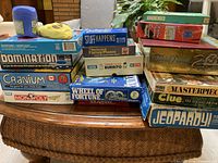 Overall view of stacked games showing titles such as Domination, Cranium, Monopoly Junior, Wheel of Fortune, Jeopardy!, Trivial Pursuit 20th Anniversary, Clue, Masterpiece and Mindbender