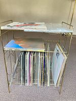 Metal rack with two shelves holding LP records and plastic sleeves on upper shelf