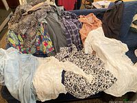 Pile of assorted tops and knit coat displayed on sofa