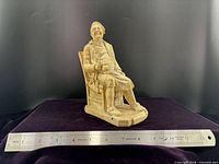 Front view of beige plaster seated man figurine with ruler for scale