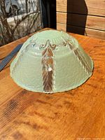 Side view of pale green pressed glass ceiling shade showing amber feather accents and texture