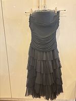 Front view of black strapless dress with ruched bodice and tiered pleated skirt