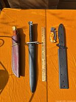 Overview of sheathed Buck knife, bayonet with scabbard, folding knife, and Smith & Wesson knife with spare sheath on orange cloth