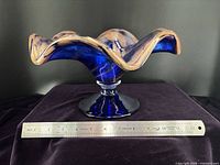 Side profile showing ruffled rim, pedestal base and ruler for scale