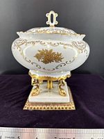 Front view of urn with lid on pedestal showing gold floral design and brass feet