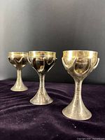 Three Rosenthal Kiddush cups standing upright showing exterior silver plating and gold interior