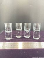 Front view of four upright shot glasses with ruler indicating height