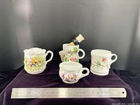 front view of four floral shaving mugs and brush with ruler for scale