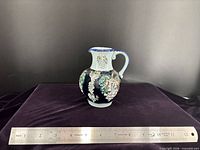 Front view of 6-in West German grapevine relief pitcher with ruler for scale