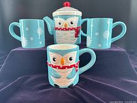 Front view of teapot and three mugs displaying owl motif and snowflakes