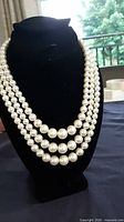 Full view of three-strand cultured pearl necklace displayed on black bust