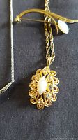 Gold-tone pendant necklace and brooch with opal-style stones, partial view of silver necklace