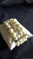 Bracelet angled on cushion showing faux pearls and rhinestone bar