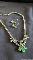 Necklace with green accents alongside matching earrings on cloth background