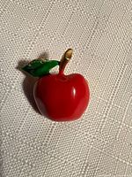 Front view of apple brooch showing red enamel body, green leaf, goldtone stem, pin back not visible