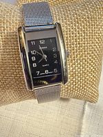 Front view of watch on cushion shows dial, case, mesh band